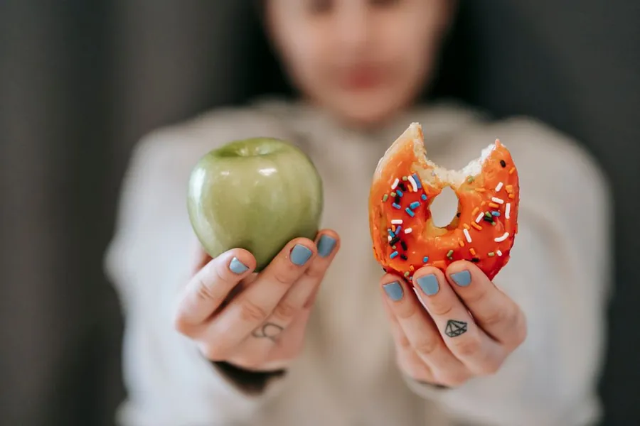 Woman holding a green apple in one hand and a bitten doughnut in the other
