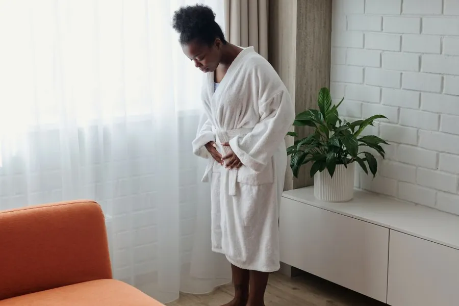 Woman in a bathrobe checking her weight on a scale at home