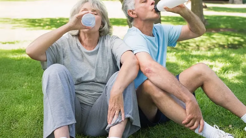 Older couple resting and drinking water in a park after exercise