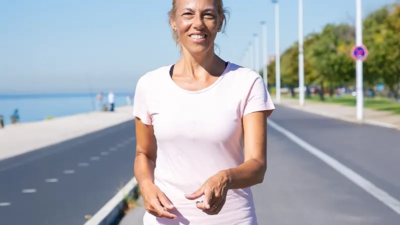 Smiling woman walking outdoors on a sunny promenade